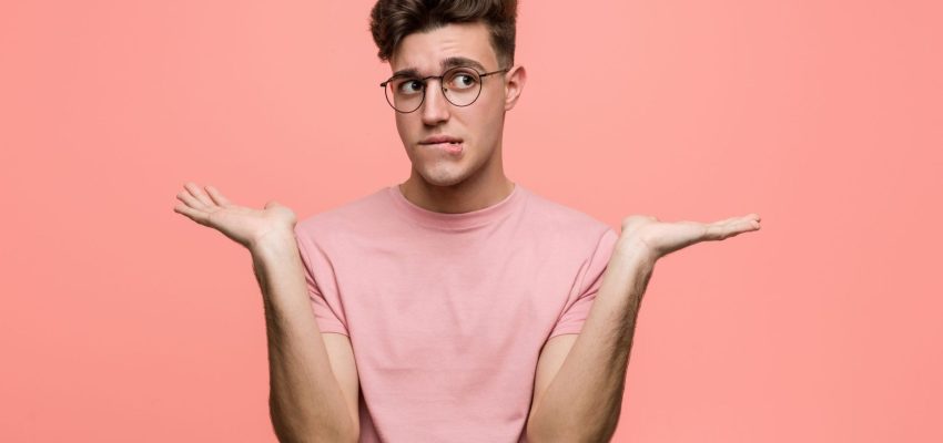 Young cool caucasian man confused and doubtful raising him hands to hold a copy space.
